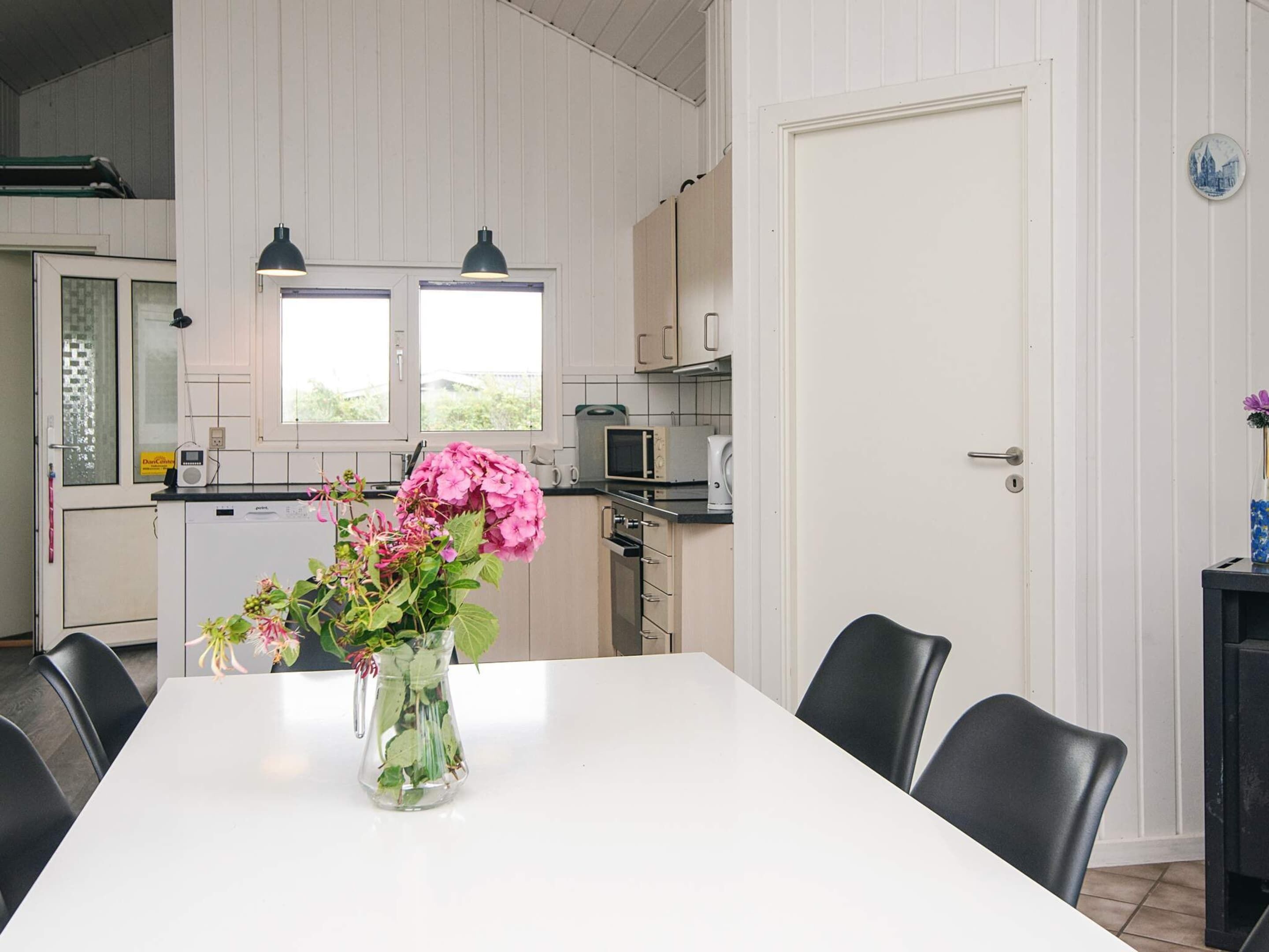 A modern kitchen with white cabinets, a microwave, and a sink. There is a dining table with chairs and a vase of flowers.