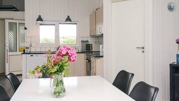 A modern kitchen with white cabinets, a microwave, and a sink. There is a dining table with chairs and a vase of flowers.