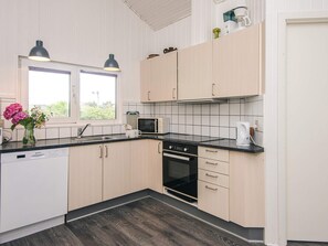 A modern kitchen with light wood cabinets, a black countertop, a dishwasher, a microwave, and a coffee maker.