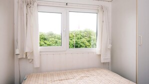 A bedroom with a bed, a window with curtains, and a view of greenery outside.