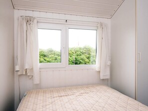 A bedroom with a bed, a window with curtains, and a view of greenery outside. - 8 Person Holiday Home in Ringkobing (Ringkobing)