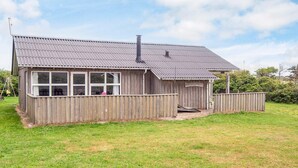 A wooden house with a metal roof, a porch, and a fenced yard. - 8 Person Holiday Home in Ringkobing (Ringkobing)