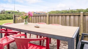 An outdoor patio with a wooden table and red plastic chairs.