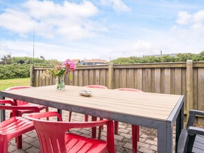 An outdoor patio with a wooden table and red plastic chairs. - 8 Person Holiday Home in Ringkobing (Ringkobing)