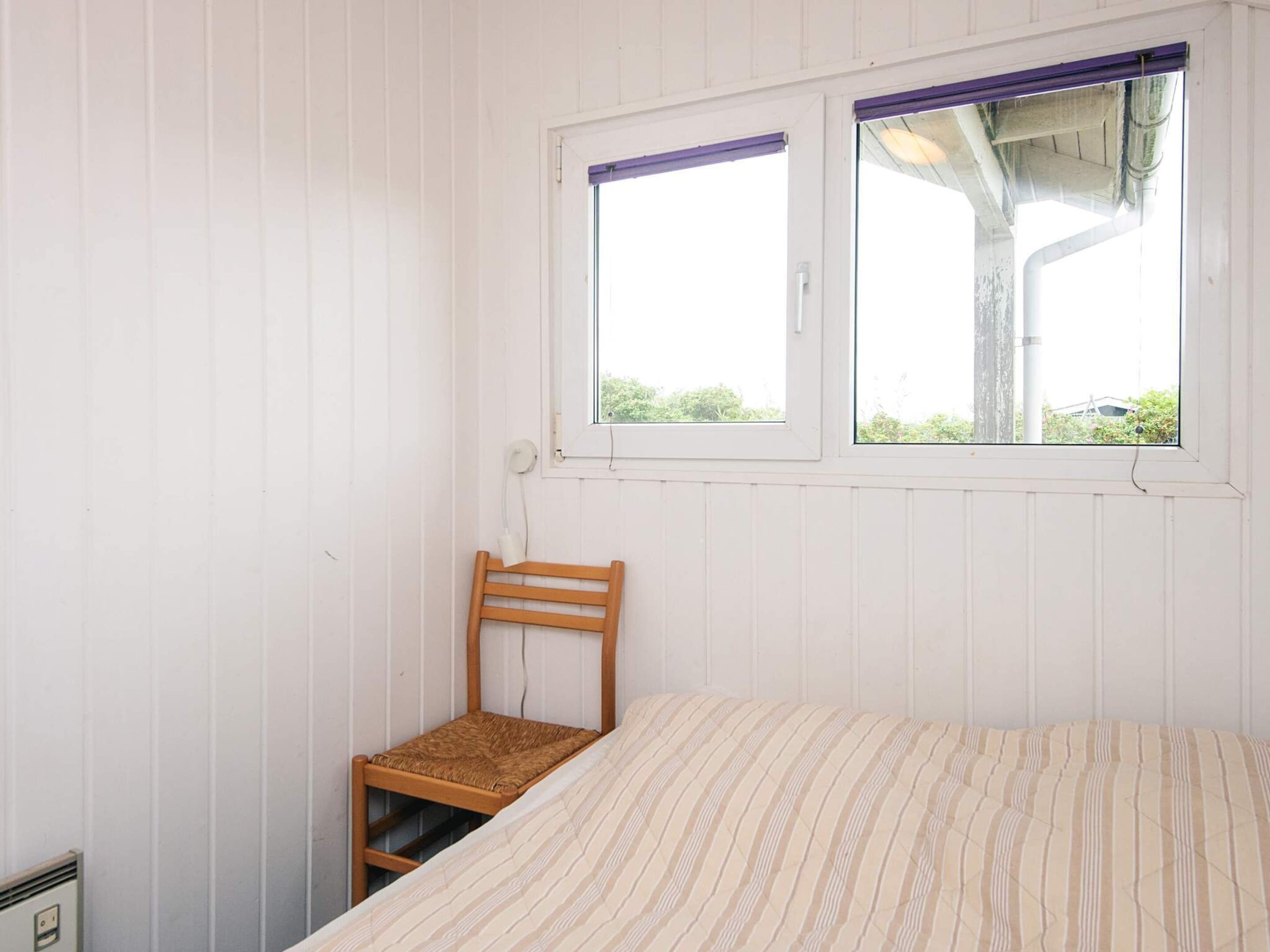 Um quarto com uma cama, janela e uma cadeira.