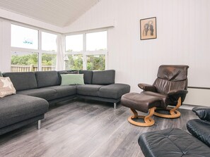 A modern living room with a sectional sofa, a leather armchair, and a black ottoman. - 8 Person Holiday Home in Ringkobing (Ringkobing)