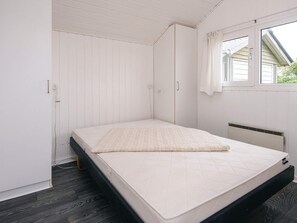 A single bed with a mattress and a pillow in a room with white walls and a window.