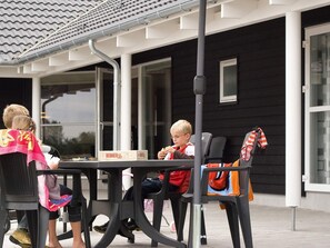 Une terrasse avec une table et des chaises, un bâtiment noir et blanc en arrière-plan et un ciel dégagé.