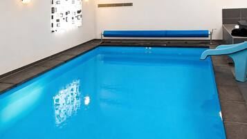 Una piscina techada transparente de color azul, con un tobogán azul y una pared con diseño geométrico.