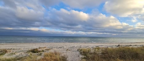 Een strandpad dat naar de oceaan leidt, onder bewolkte luchten.