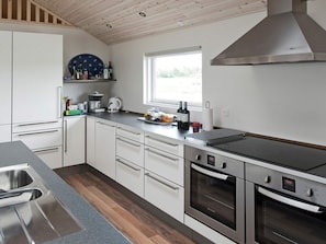 A modern kitchen with white cabinetry, a stainless steel sink, a built-in oven, and a window providing natural light.