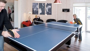 A ping pong table in a room with wooden walls, two pendant lights, and framed pictures on the wall.