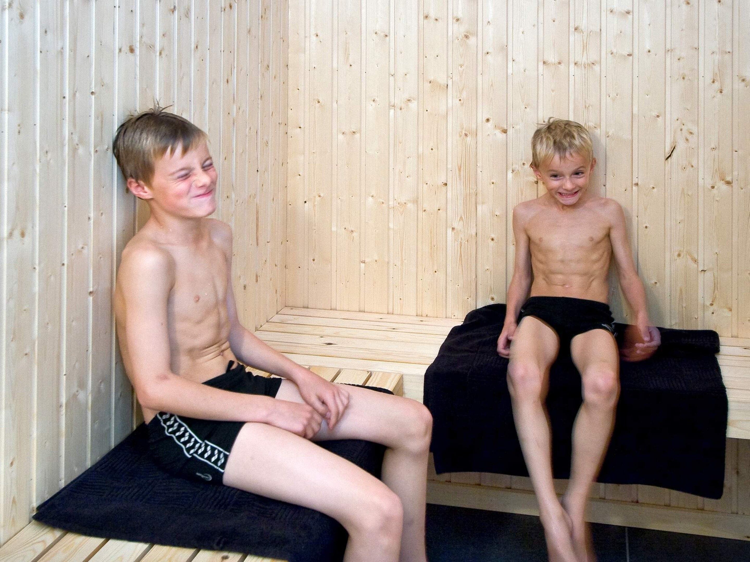Two individuals seated in a sauna with wooden walls and benches.
