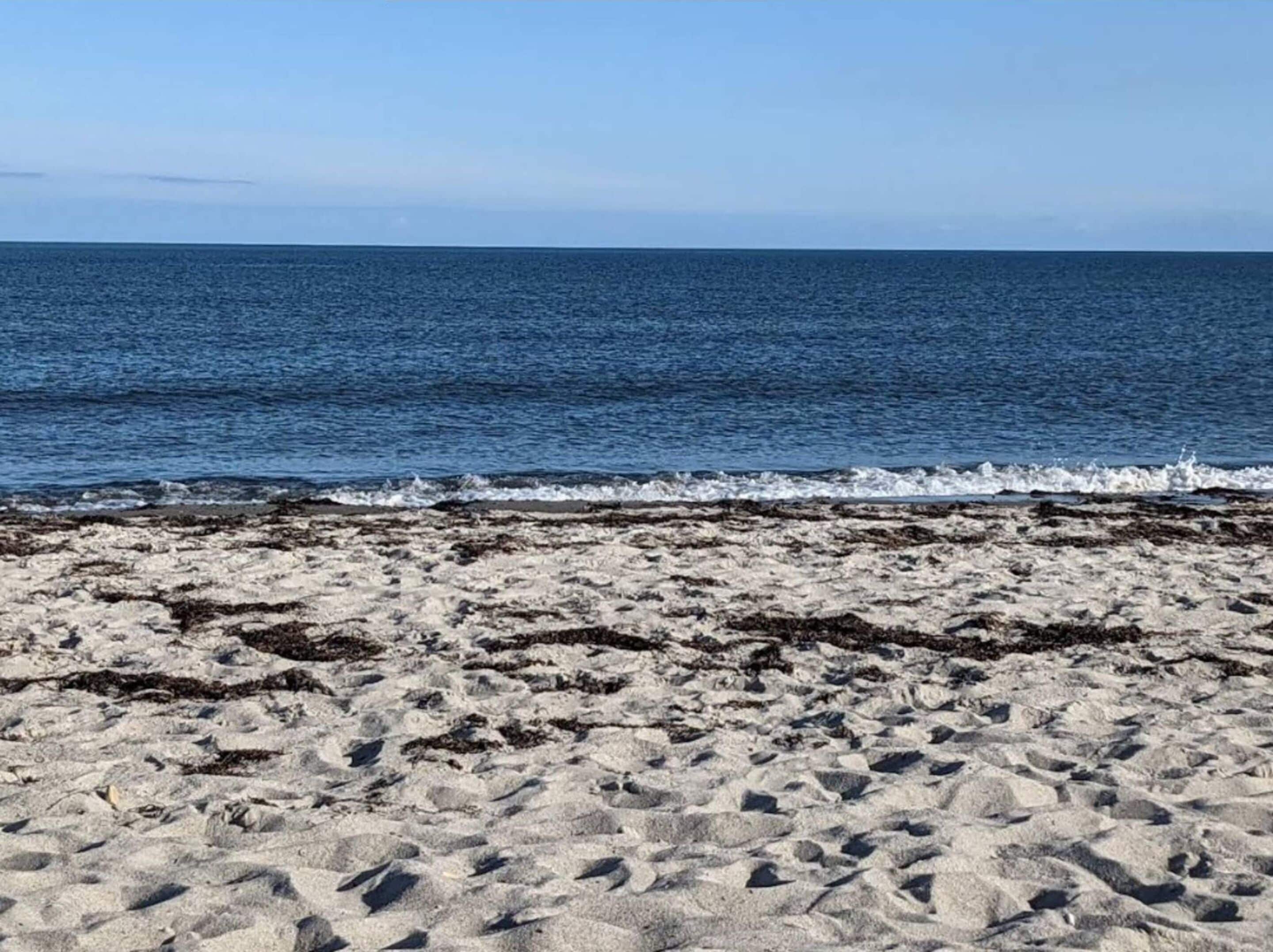 Ein sandiger Strand mit ankommenden Wellen.