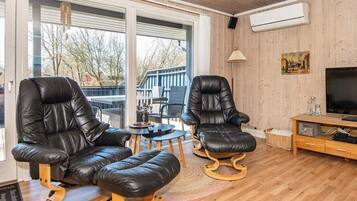 Un salon moderne avec deux fauteuils en cuir noir, une table basse en bois et un téléviseur posé sur un meuble en bois.