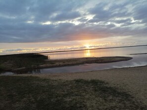 A natural landscape with a body of water reflecting the sky, surrounded by grassy areas and a distant horizon.