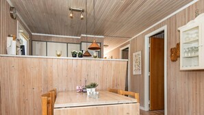 A wooden dining table with chairs, a hanging light fixture, and a kitchen area with wooden paneling. - 6 Person Holiday Home in Hemmet (Hemmet)