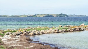 A coastal landscape with a rocky shoreline, calm water, and distant hills. - Stylish Holiday Home in Føllenslev near Sea (Follenslev)