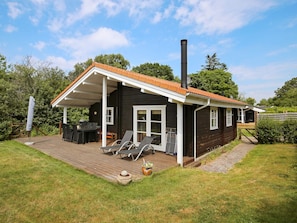 Una cabaña con terraza, mobiliario exterior y chimenea.