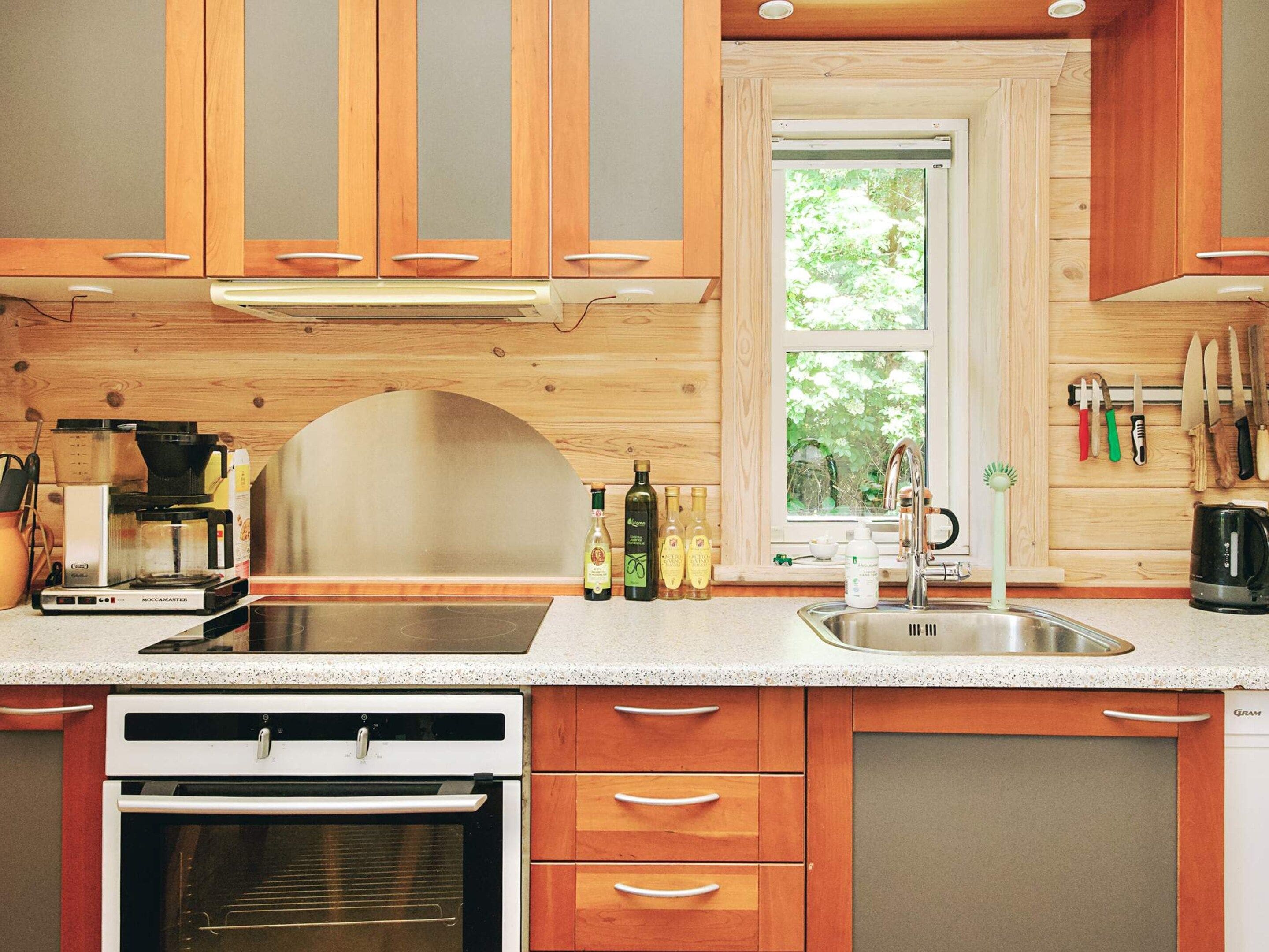 A modern kitchen with wooden cabinets, a built-in oven, a coffee machine, and a window with a view of greenery.