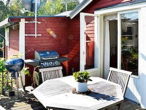 A wooden deck with a barbecue grill, a grill cover, and a table with chairs.