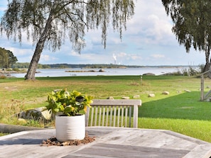 A wooden table with a potted plant, a bench, and a view of a lake with trees and distant structures.