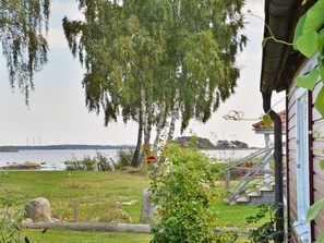 A lakeside property with a wooden deck, a stone wall, and a view of the water. - Holiday Home in Sölvesborg (Sölvesborg)