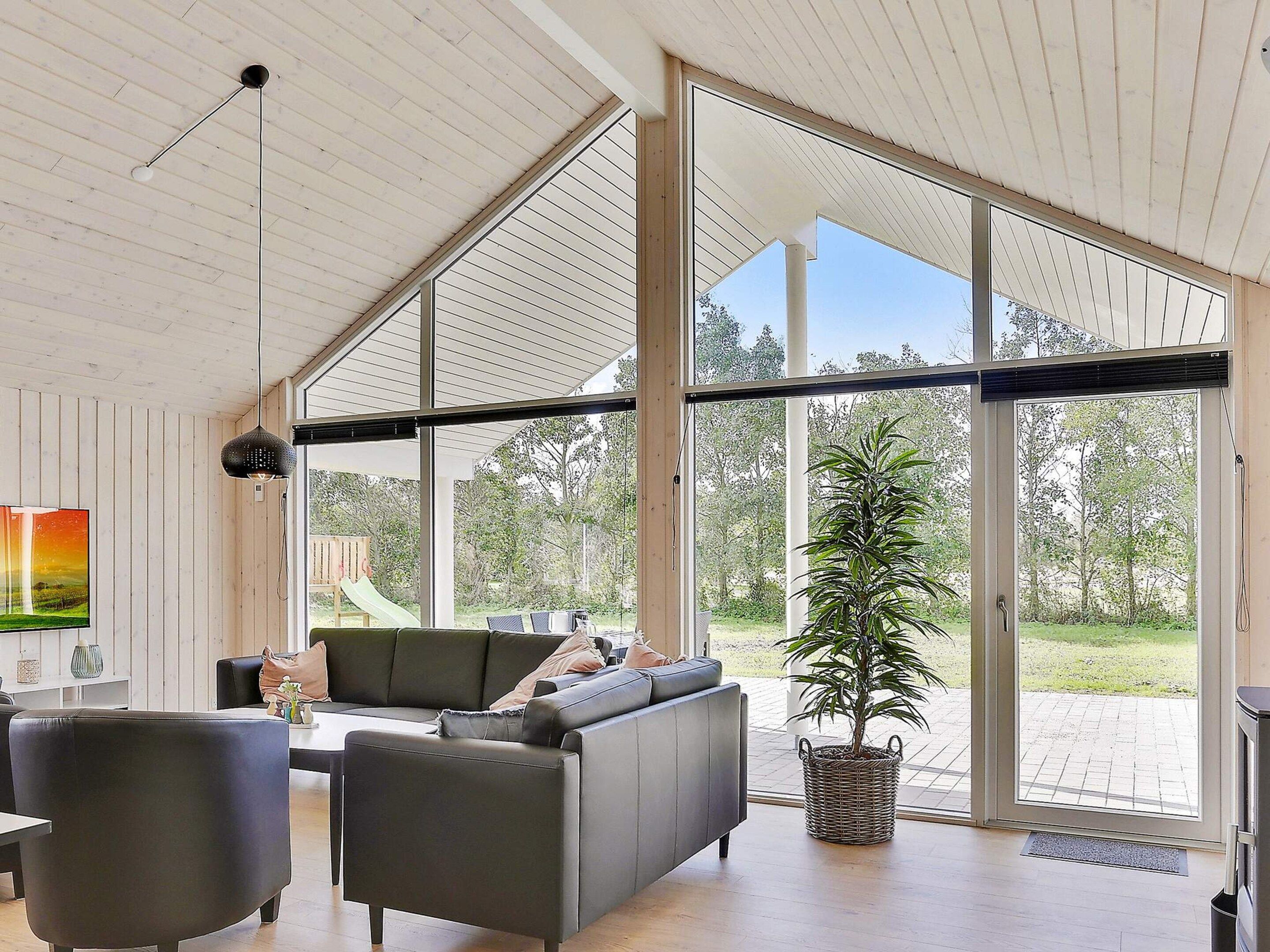 A modern living room with a large window, a sofa, a dining table, and a potted plant.