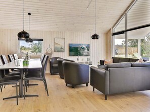 A modern living room with a dining area, large windows, and a flat-screen TV.