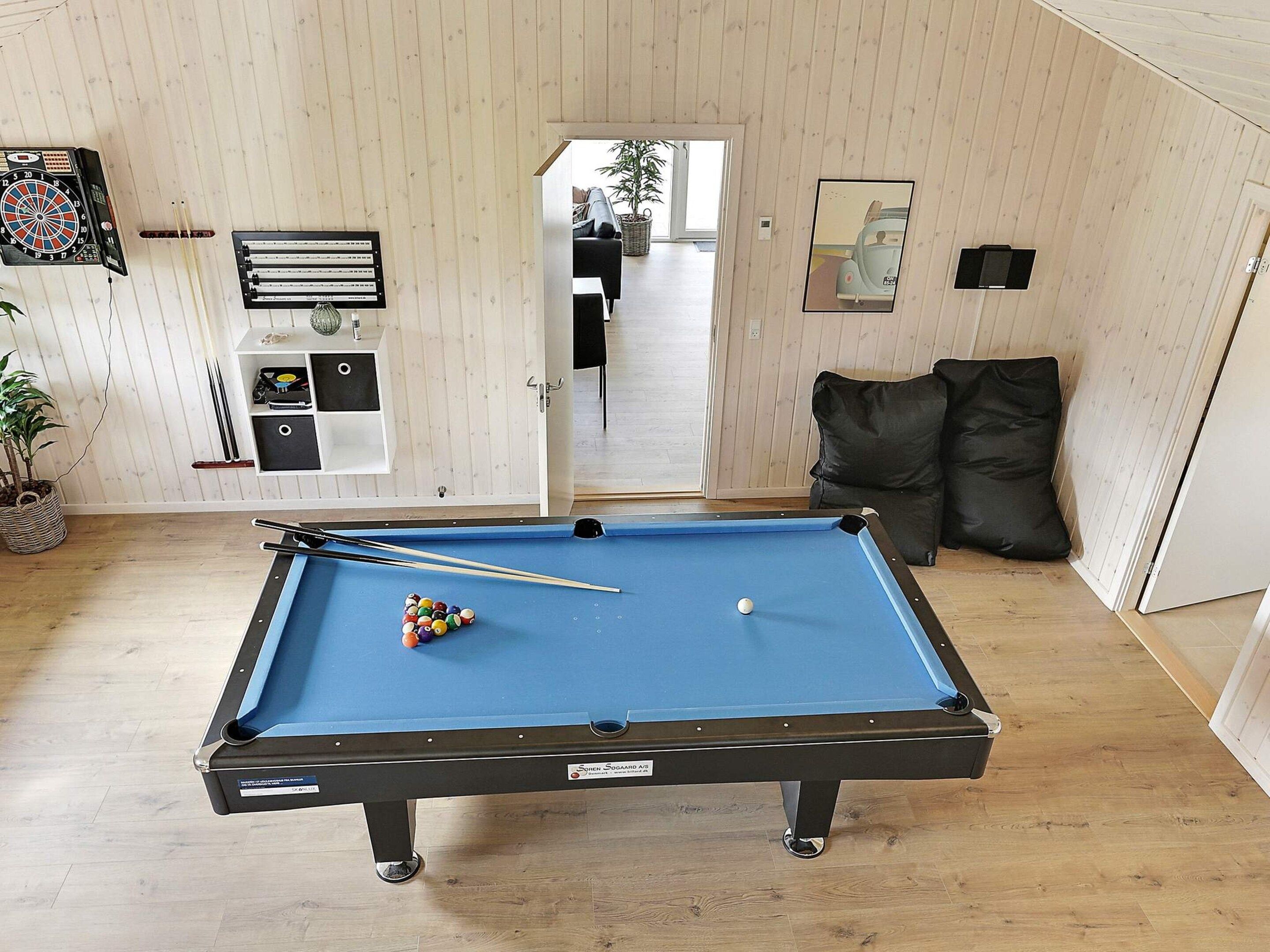 A pool table with balls, a dartboard, and a framed picture on the wall.