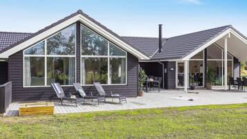 Een modern huis met grote ramen, een terras met tuinmeubilair en een schoorsteen.