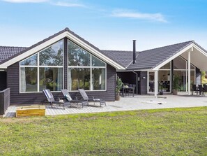 Una casa moderna con ventanas amplias, un patio con mobiliario exterior y una chimenea.