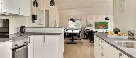 A modern kitchen with white cabinetry, a built-in oven, a dining area with a table and chairs, and a fruit bowl on the counter.