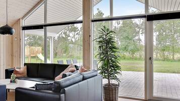 A modern interior with a sectional sofa, a dining table, and a large window offering a view of the outdoors.