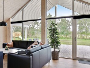 A modern interior with a sectional sofa, a dining table, and a large window offering a view of the outdoors. - 5 Star Holiday Home in Idestrup (Idestrup)