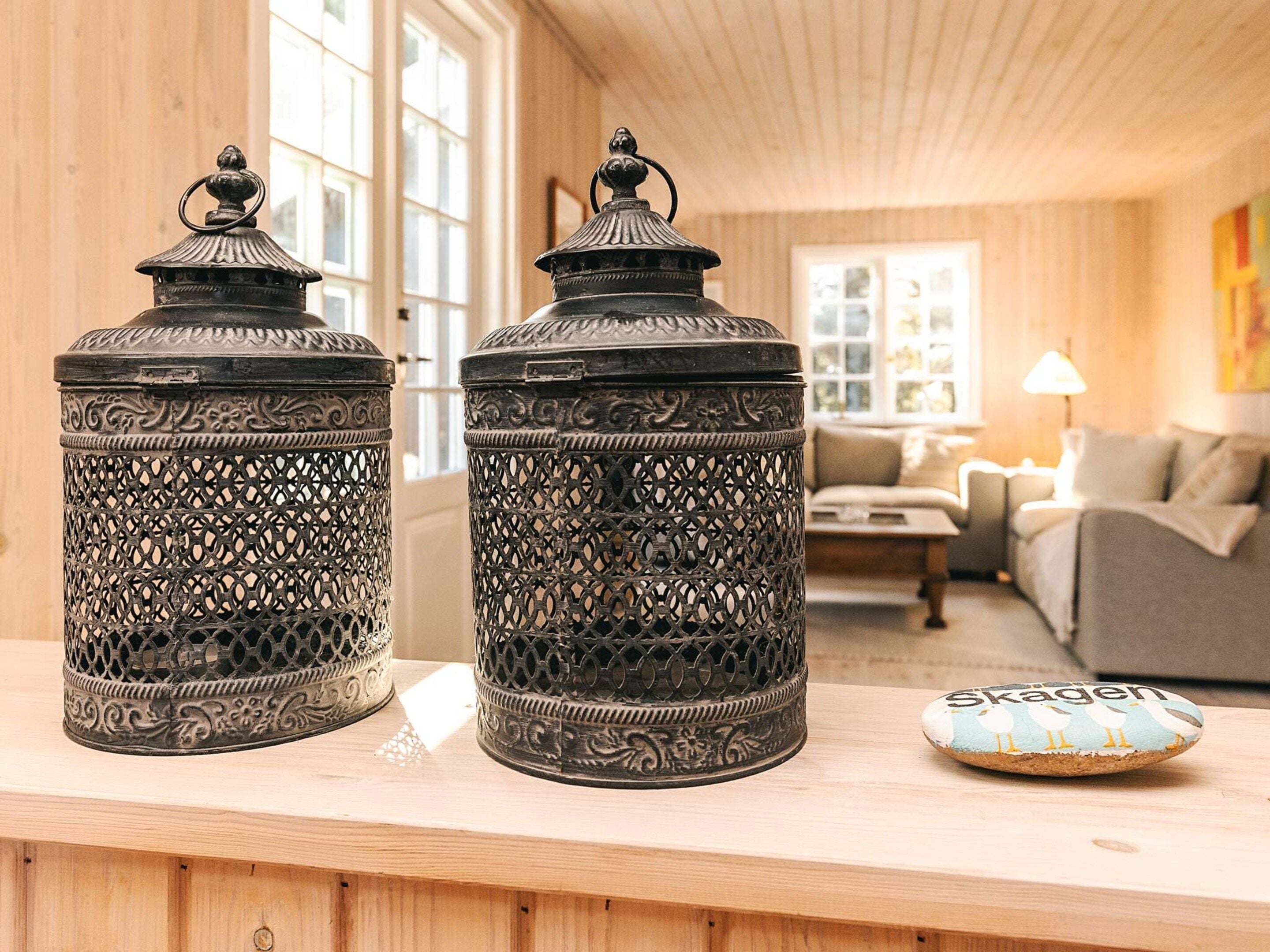 Deux lanternes en métal décorées sont posées sur une étagère en bois, dans une pièce où se trouvent un canapé et une lampe.