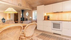 A cozy kitchen with wooden cabinets, a dining area with wicker chairs, and a fireplace. - 4 Person Holiday Home in Skagen (Skagen)