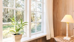 A room with a large window, a potted plant, a lamp on a small table, and a wicker basket. - 4 Person Holiday Home in Skagen (Skagen)