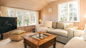 A cozy living room with a wooden ceiling, a sofa, a coffee table, and large windows with curtains. - 4 Person Holiday Home in Skagen (Skagen)