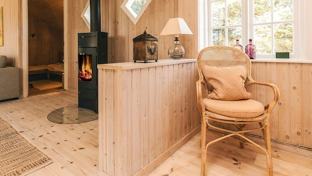 A cozy room with a wood-burning stove, a wicker chair, a window with a view, and a small table with a lamp. - 4 Person Holiday Home in Skagen (Skagen)