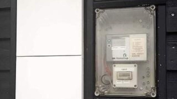 Caja de contadores con una etiqueta y un dispositivo más pequeño en su interior, fijada a la pared.
