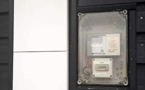 A utility meter box with a label and a smaller device inside, mounted on a wall.