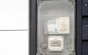 A utility meter with a label and a digital display, mounted on a metal frame.
