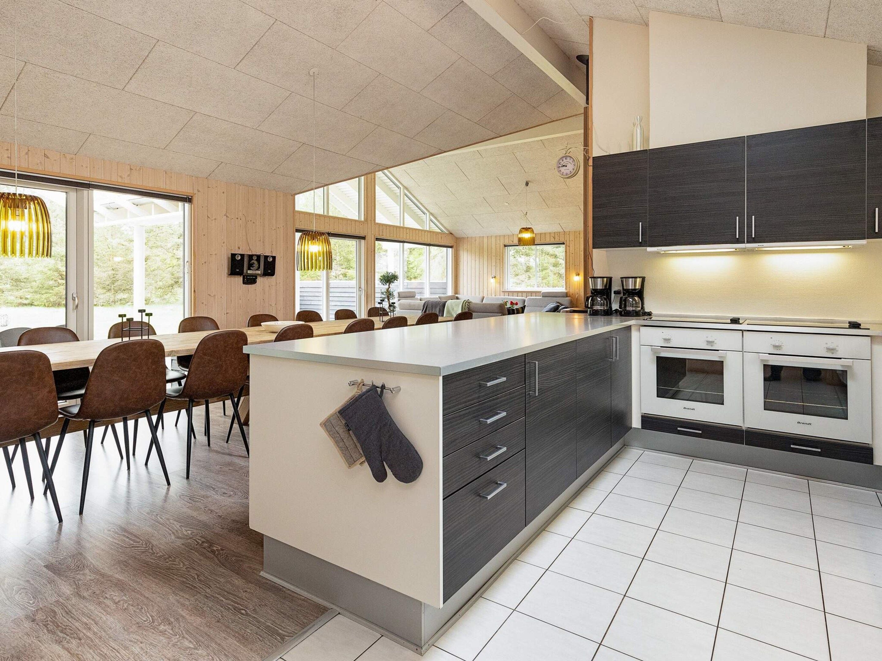 A modern kitchen with a central island, built-in appliances, and a dining area with wooden tables and chairs.