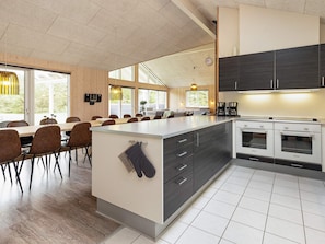 A modern kitchen with a central island, dark cabinets, and a dining area with wooden chairs.