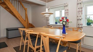 Un coin repas avec une table en bois, des chaises, un vase de fleurs, un escalier et une fenêtre avec des rideaux.