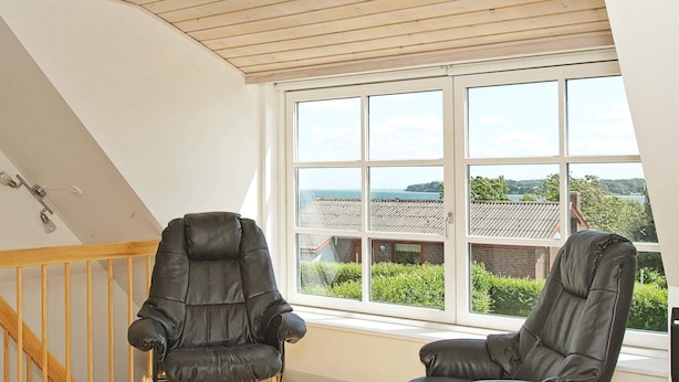 Une pièce avec deux fauteuils en cuir, un escalier en bois et une grande fenêtre donnant sur un paysage.