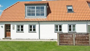 Une maison de plain-pied avec un toit recouvert de tuiles rouges, des murs extérieurs blancs et une petite fenêtre au deuxième étage.