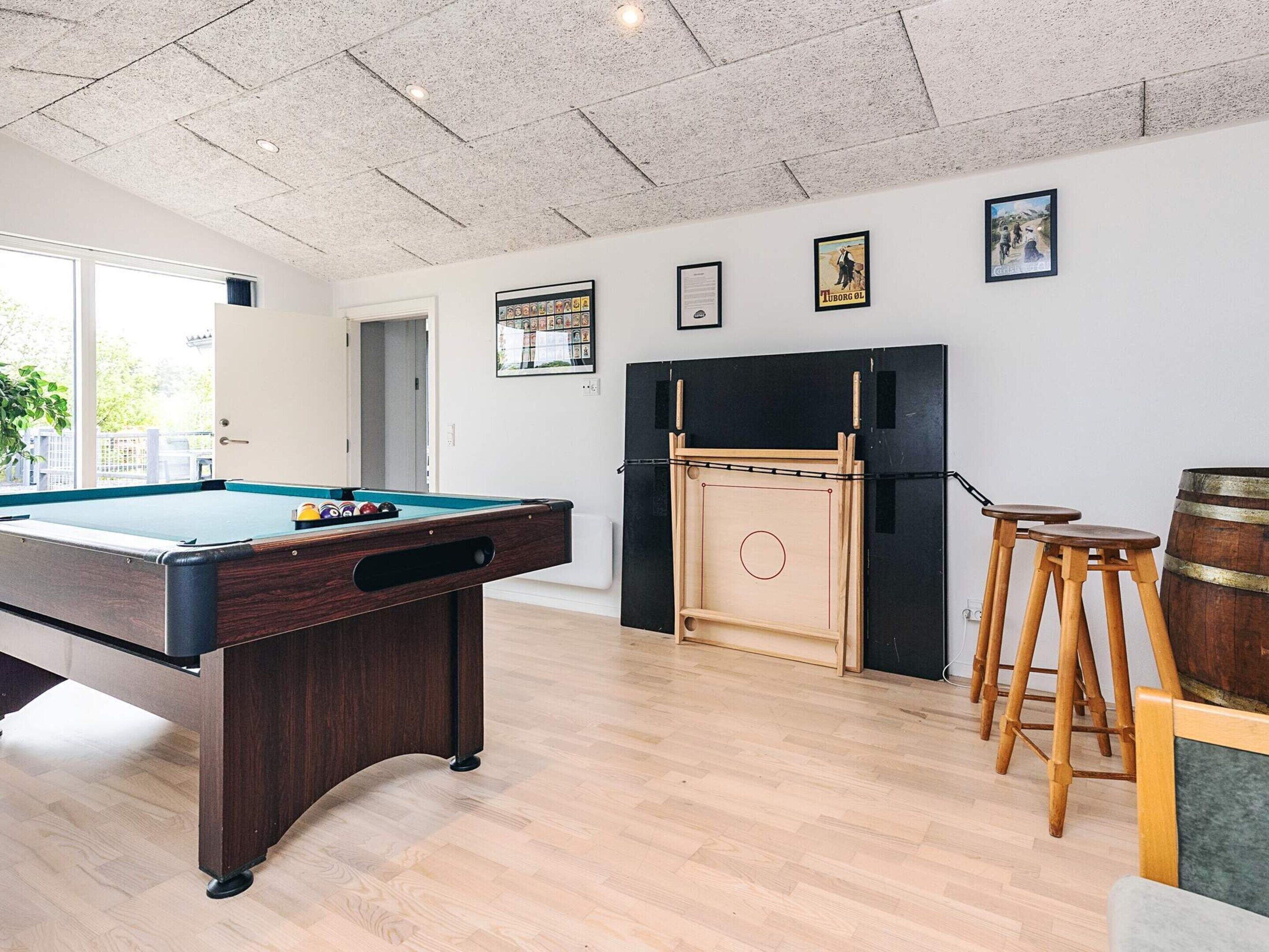 A pool table in a room with wooden flooring, a fireplace, and framed pictures on the wall.