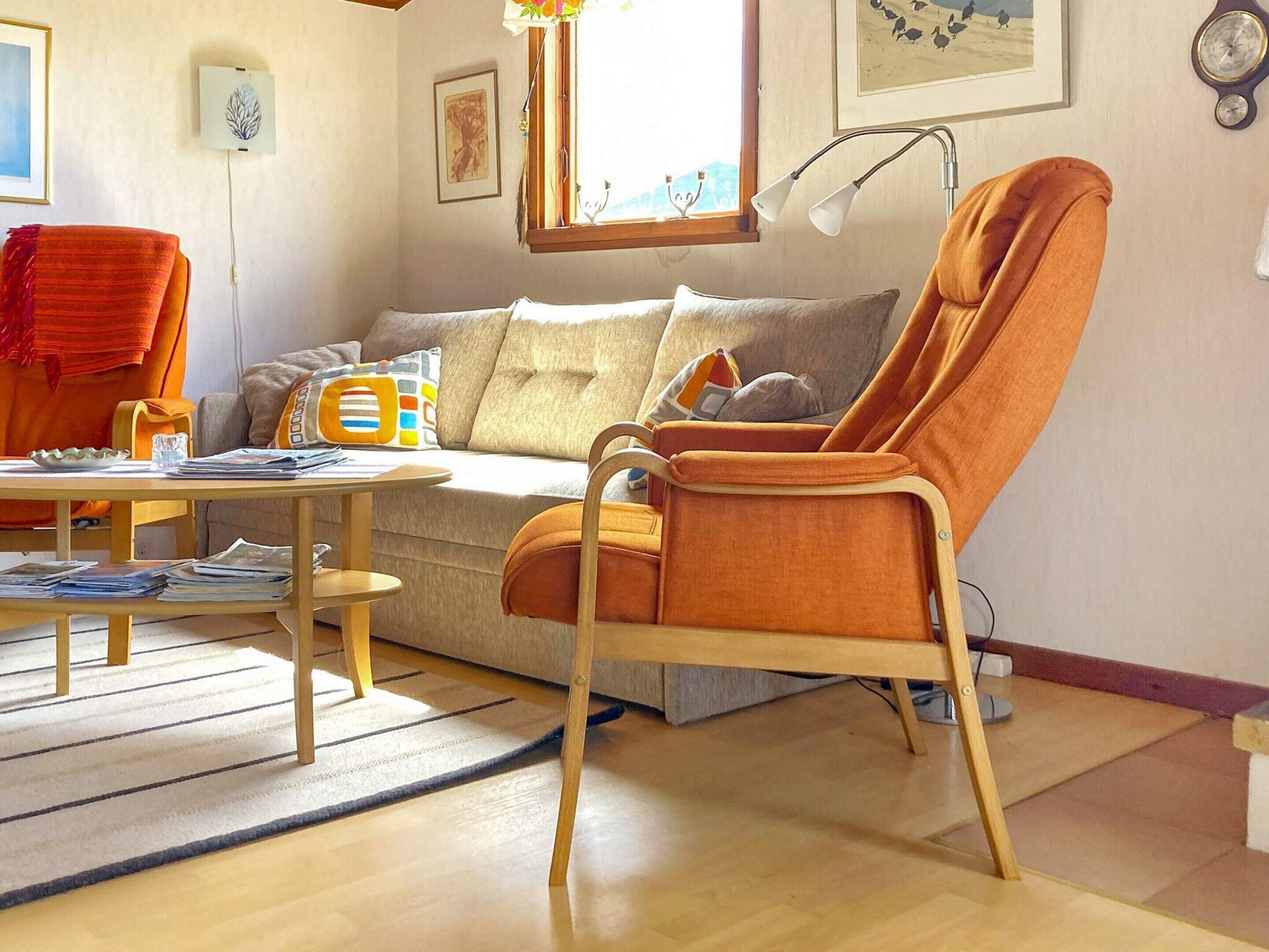 Ett vardagsrum med en soffa, ett soffbord i trä, en fåtölj med högt ryggstöd och en lampa.